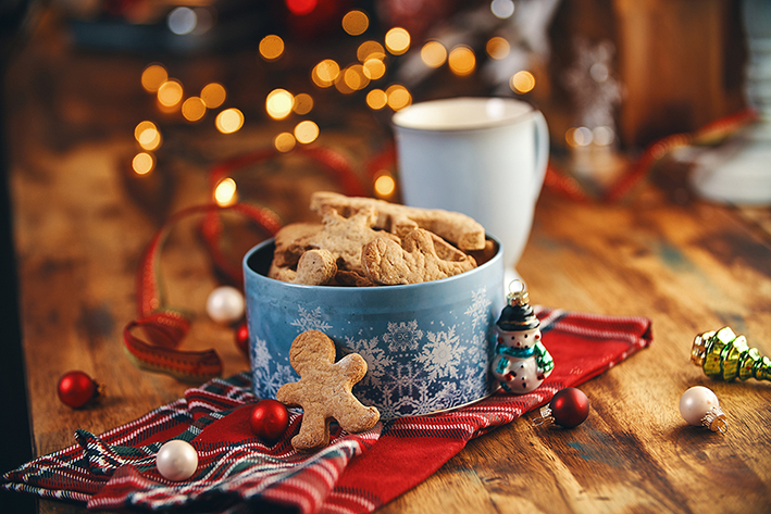 Nybakade pepparkakor och varm choklad. Julfika med julbelysning och dekorationer i bakgrund.